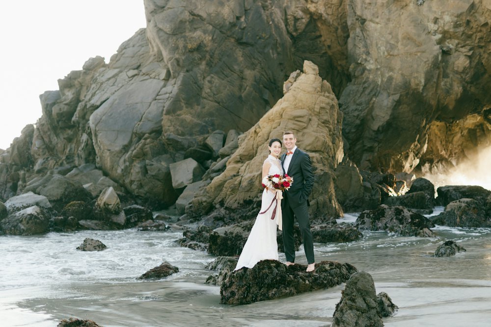 Bride and groom standing on rocks by the sea
